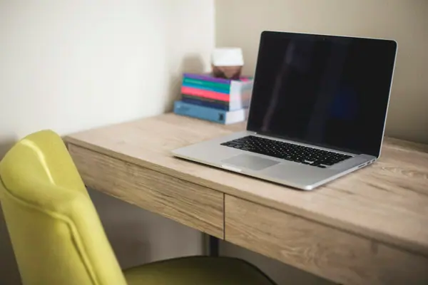 A laptop and books on a wooden desk beside a green chair